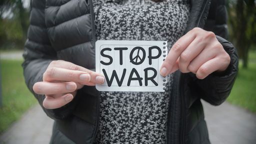 A closeup shot of a woman in the middle of a park holding a paper with the message of Stop War