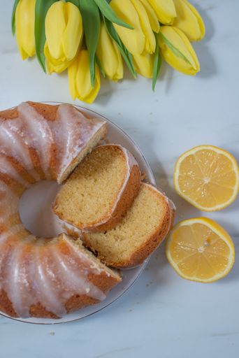 A vertical top view of the vanilla pound cake with lemon and yellow tulips on the marble table