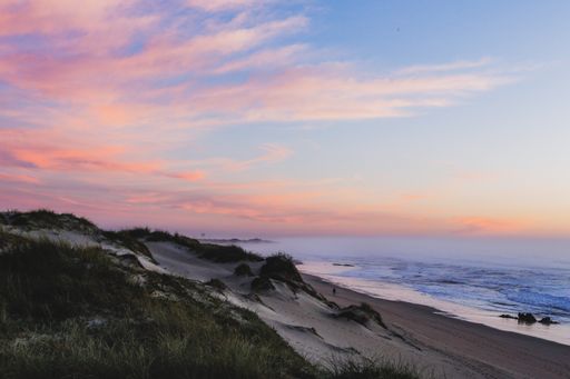 A scenic view of a shore and a body of water at sunset with colorful clouds in the sky