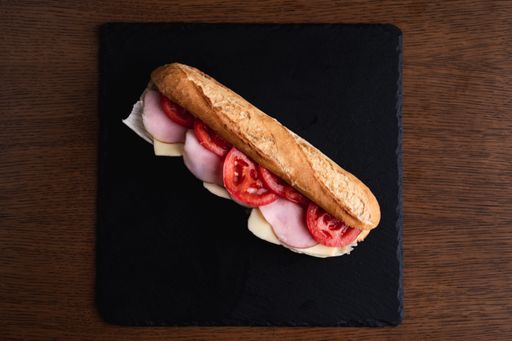 A top view of a delicious sandwich with slices of sausage, tomatoes and cheese placed on a black surface on the table