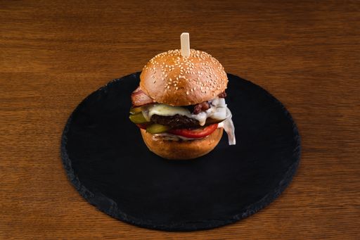 A top view of a hamburger with juicy beef, pickles, pepper, and cabbage on a black wooden surface