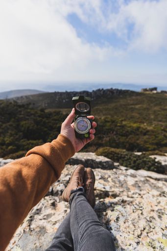 A vertical shot of a hand holding a compass and the hills in the background