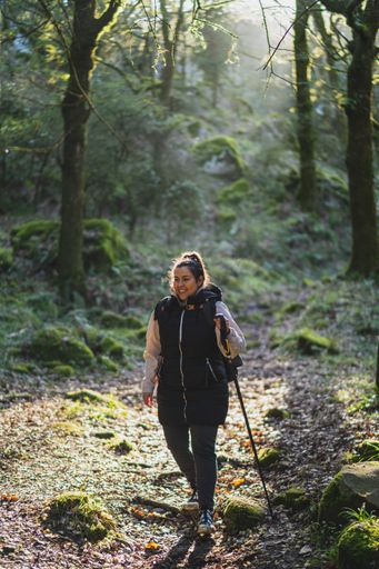 A vertical shot of a young female with a walking stick during the hike in the lush green forest