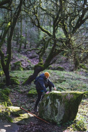 A vertical shot of a male trying to stand on a big mossy rock  in the lush green forest during the hike