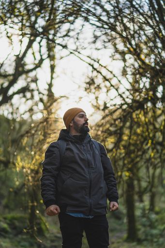 A vertical shot of a male in a forest during the hike with the background of the sun behind trees