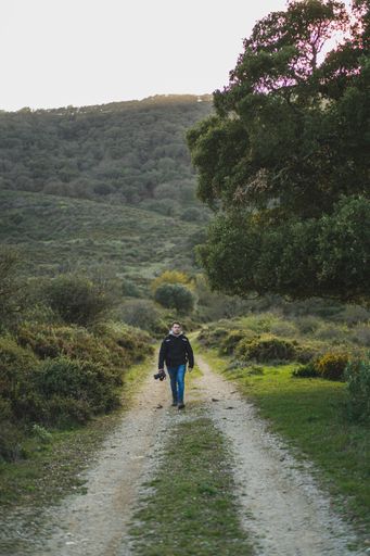 A vertical shot of a young male with a camera walking on a mountain trail during the hike