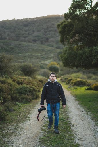 A vertical shot of a young male with a camera walking on a mountain trail during the hike
