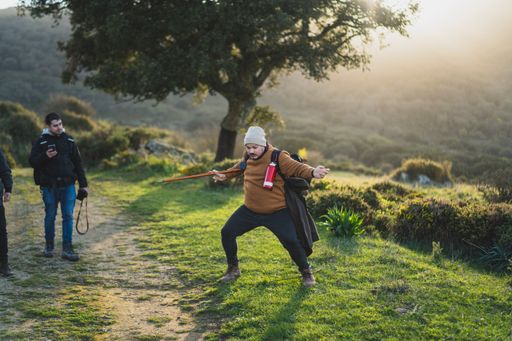 A male with a stick and equipment for hiking on a green path with the sun behind the mountains