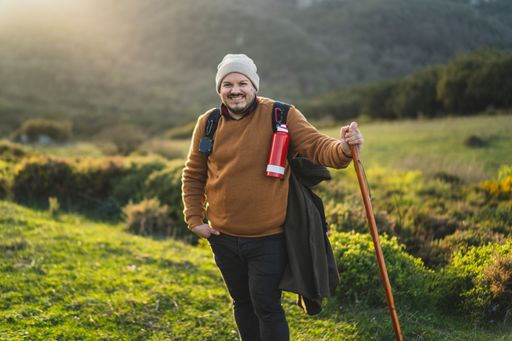 A male with a stick and equipment for hiking on a green path with the sun behind the mountains