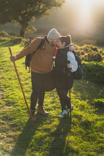 A vertical shot of a couple taking pictures on a green mountain path during the hike on a sunny day