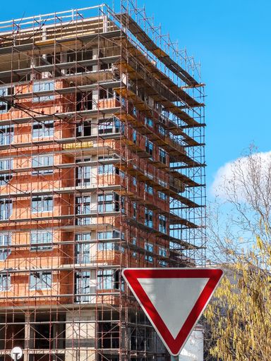 Apartment building construction site with scaffolding and crane against blue sky