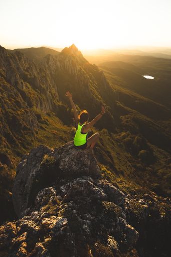 A vertical shot of a female sitting on a rock with arms raised during sunset