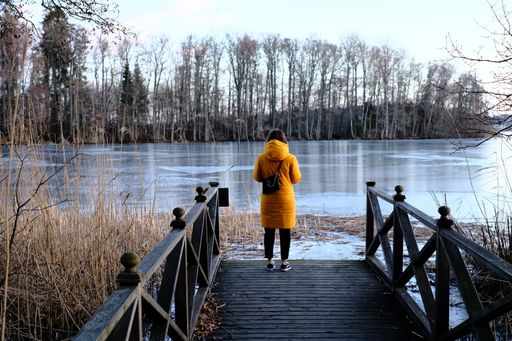 A girl with yellow coat looking at frozen lake and trees in Sweden on the bridge