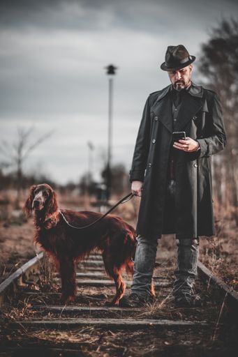 A vertical shot of a Swedish man with a cocker spaniel standing on a railway.