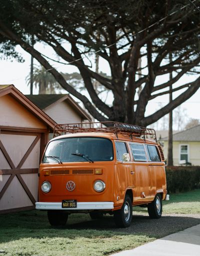 A vertical shot of an orange VW classic van parked in a park