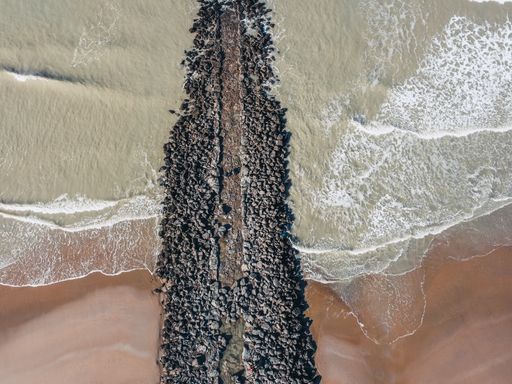 An aerial view of the wavy North Sea hitting the sandy beach