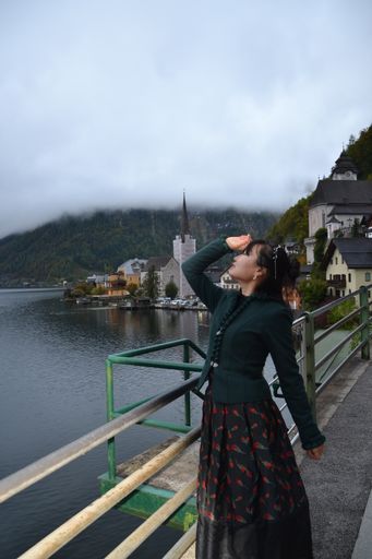 A vertical shot of a Chinese female posing by the green railings near the water in Hallstatt, Austria
