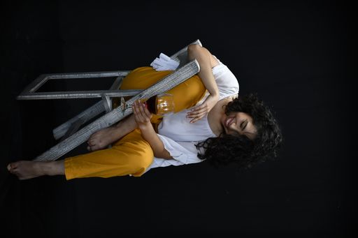 A vertical shot of a Hispanic female posing with a glass of wine in front of a black background