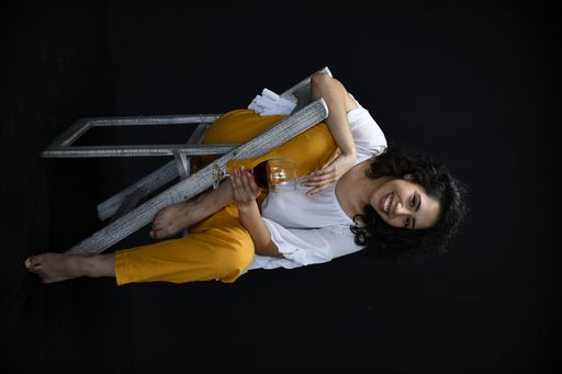 A vertical shot of a Hispanic female posing with a glass of wine in front of a black background