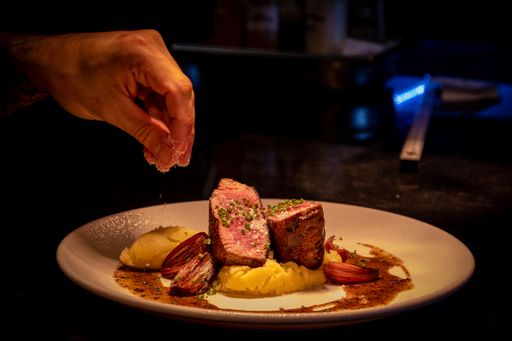 A closeup of a male hand adding pinch of seasoning on a steak on the plate in the restaurant