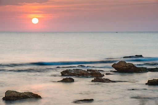 A horizontal shot of a body of water with rocks near the shore during sunset