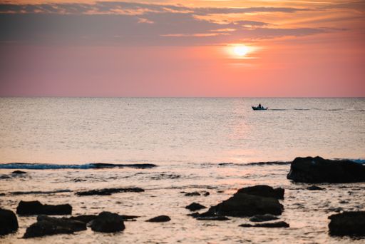 A horizontal shot of a body of water with rocks near the shore during sunset