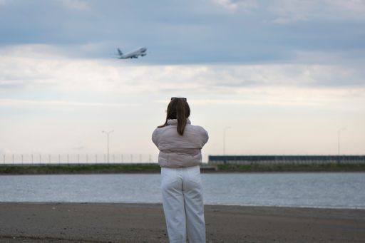 A back view of a female looking at the flying airplane over the sea