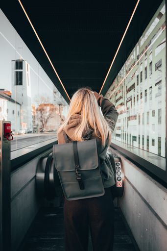 A vertical back view of a blonde female with a backpack going on an escalator