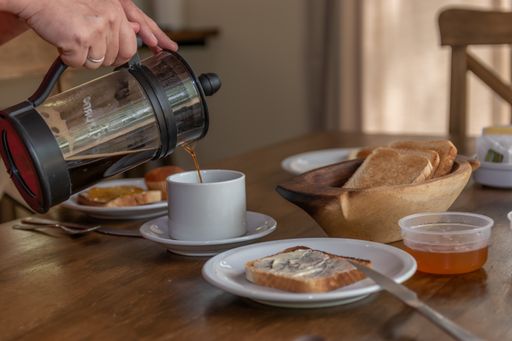 A person pouring tea into the cup next to the bread, honey, and other breakfast items