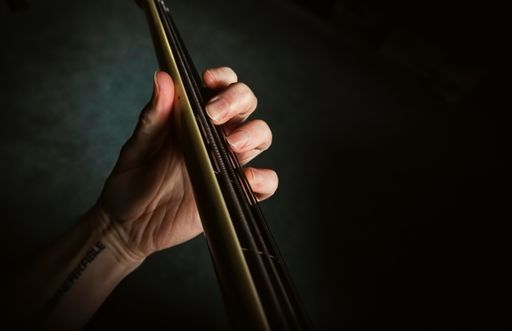 A musician’s hand on neck and fretboard of a fretless electric bass guitar