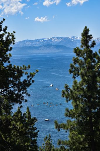 A vertical distant shot of boats floating on the body of a blue sea surrounded by mountains and trees
