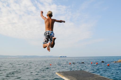 A back view of a young male jumping from  the platform into the blue sea