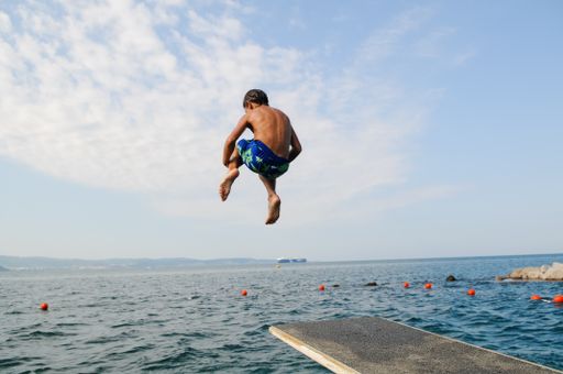 A back view of a young male jumping from  the platform into the blue sea