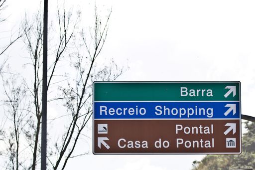 A road signboard in green, blue and red colors with arrows and writings