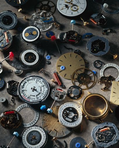 A vertical high angle shot of parts of dismantled watches on a gray surface