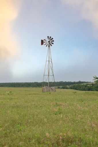 A vertical shot of an old windmill in the countryside against a blue cloudy sky