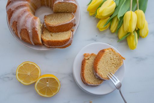 A top view of a traditional vanilla pound cake with lemons and yellow tulips on a table