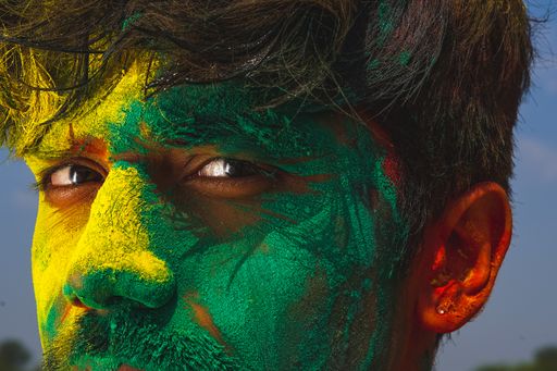 A portrait of a young Indian male covered in yellow and green holi colors