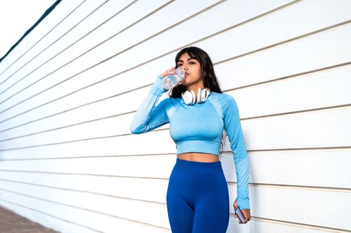 A Attractive Colombian woman taking a break to drink water while doing sports in a park