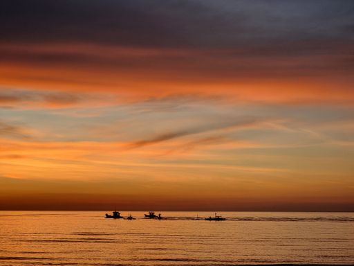 A silhouette shot of lined fishing boats on the sea during golden sunset