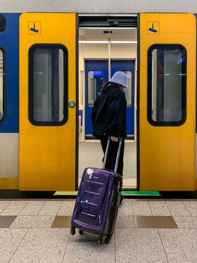 A back shot of a Girl carrying a purple suitcase entering a metro wagon in Amsterdam, Netherlands