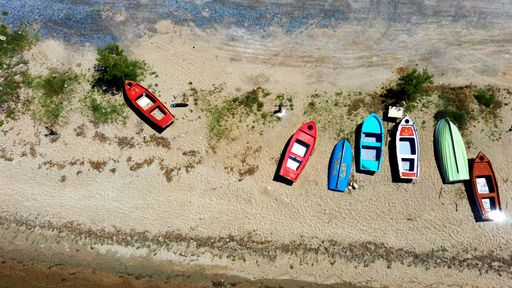 An aerial overhead shot of colorful boats on the sand near the sea