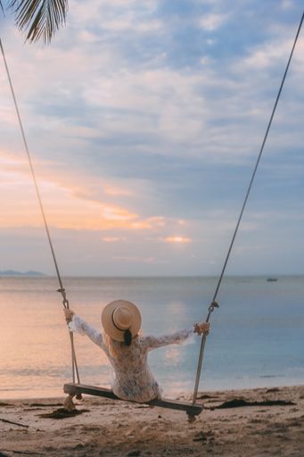 A vertical shot of a swinging Polish girl in a beach with palm trees