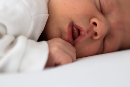 The newborn calmly sleeping baby in a white clothes on a white blanket