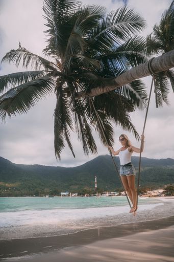 A vertical shot of a swinging Polish girl in a beach with palm trees
