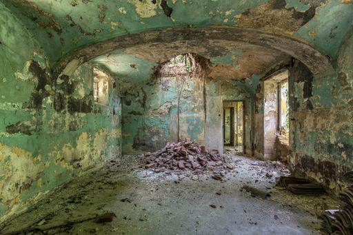 An interior shot of an abandoned building interior with green walls and collapsed ceiling