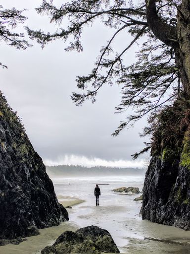 A horizontal shot of a woman standing in between cliffs looking at waves in a body of water