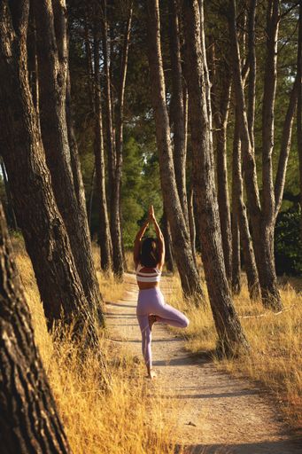 A vertical shot of a young woman doing yoga in a narrow pathway in a forested area