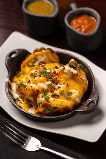 A vertical close-up shot of a Mexican potato dish with cheddar cheese and scallions.