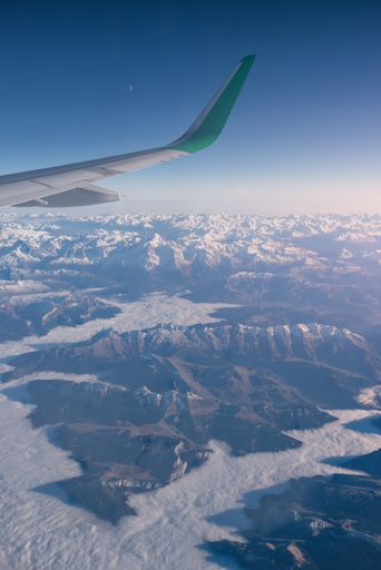 An aerial shot of the snow-capped mountains with an airplane green winglet on the foreground